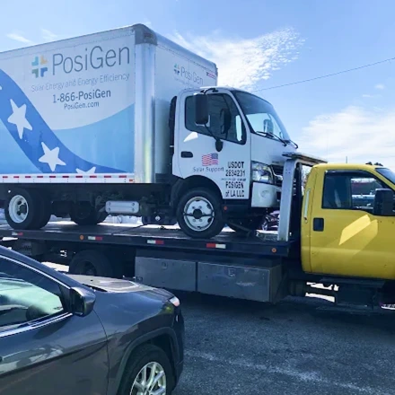 Commercial box truck loaded onto a flatbed tow truck for vehicle transport in a parking area.