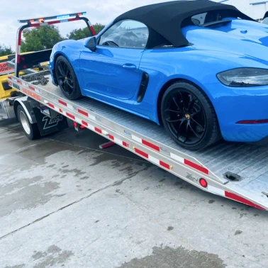 Blue convertible sports car secured on a flatbed tow truck during vehicle transport.