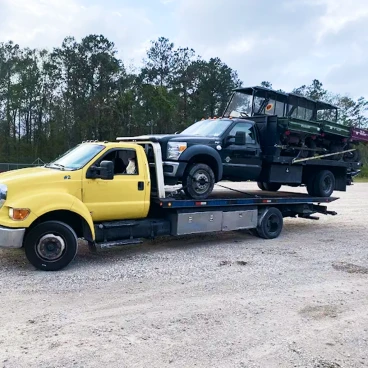 Flatbed tow truck transporting a utility truck on a gravel roadside area, showing professional vehicle recovery and transport.