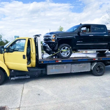 Black pickup truck secured on a flatbed tow truck during roadside vehicle transport.