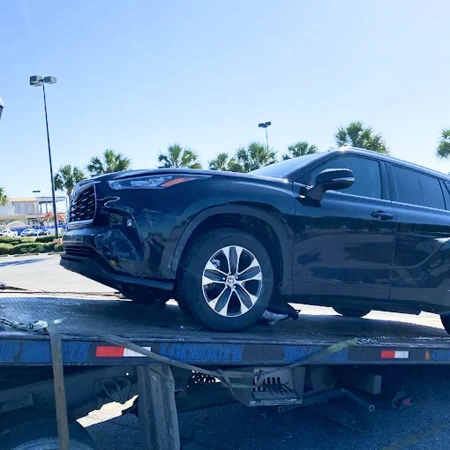 Black SUV positioned and secured on a flatbed tow truck at a roadside location for vehicle transport.