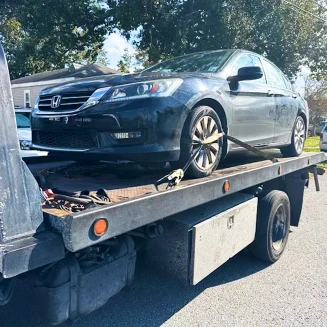 Sedan secured on a flatbed tow truck during daytime roadside vehicle transport.