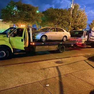 Sedan secured on a flatbed tow truck during nighttime roadside vehicle transport.